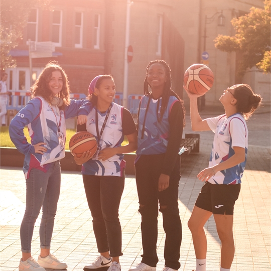 Four students laughing and smiling outside with a basketball