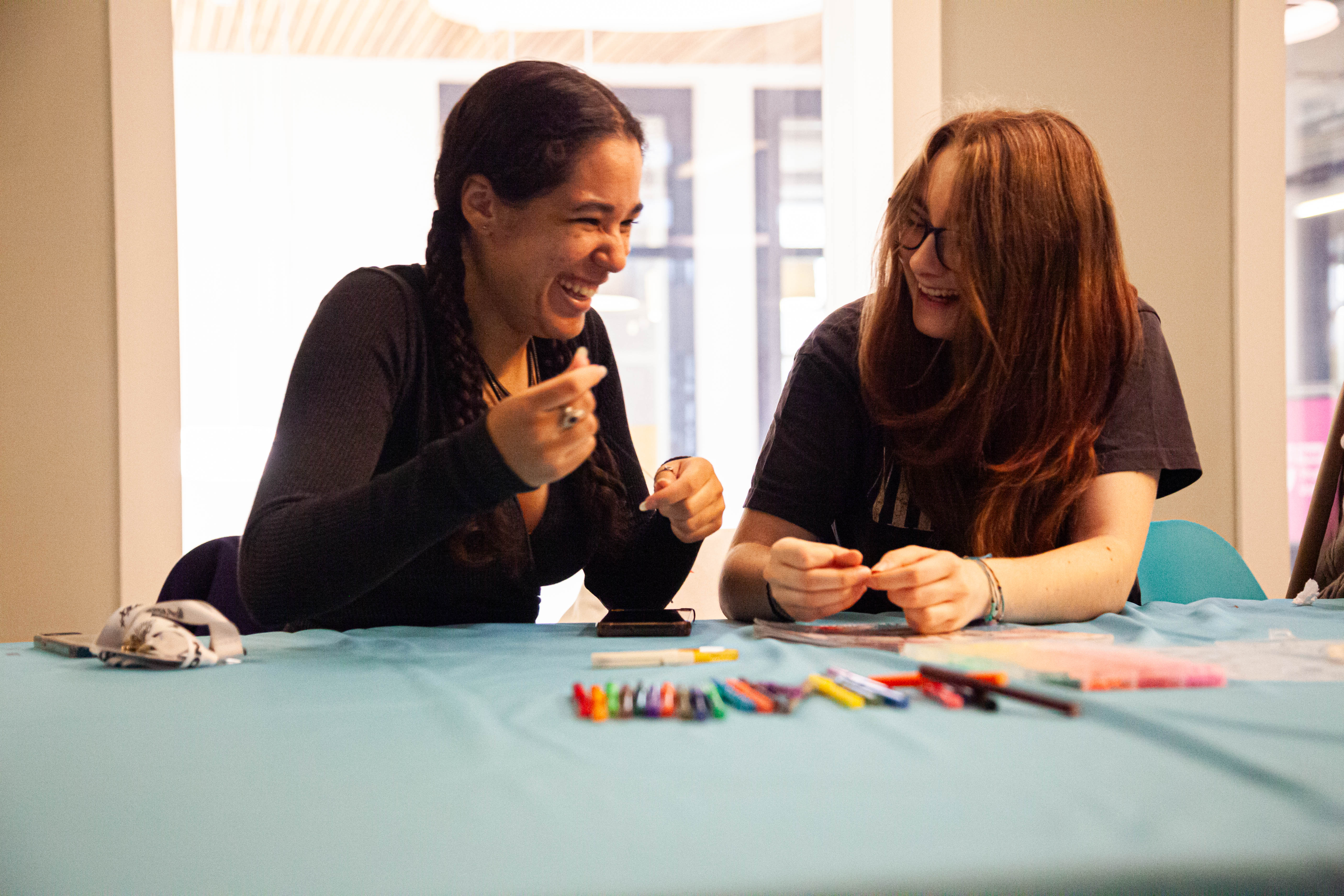 Two people looking at each other laughing while sat at a table.