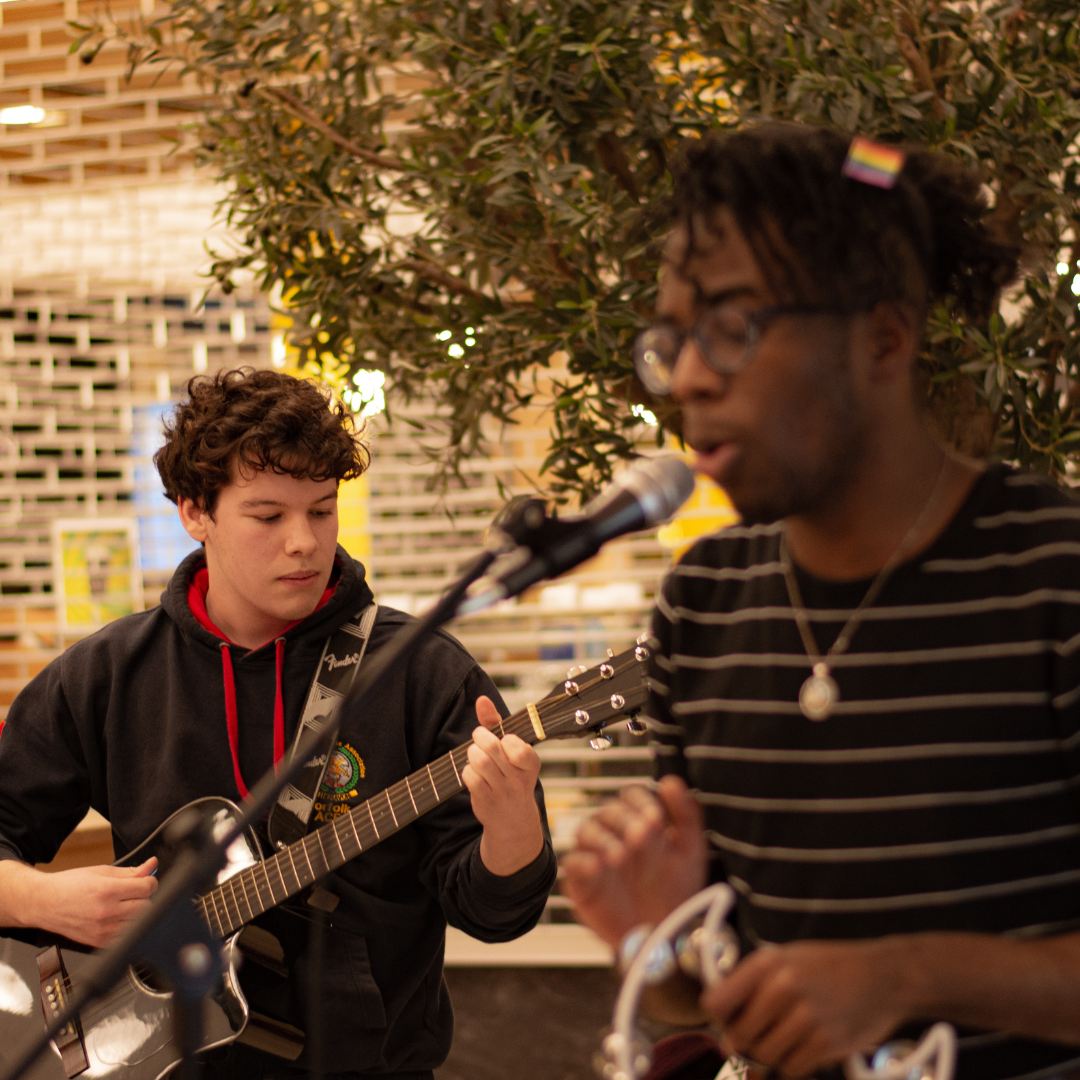A student playing guitar with another student singing.