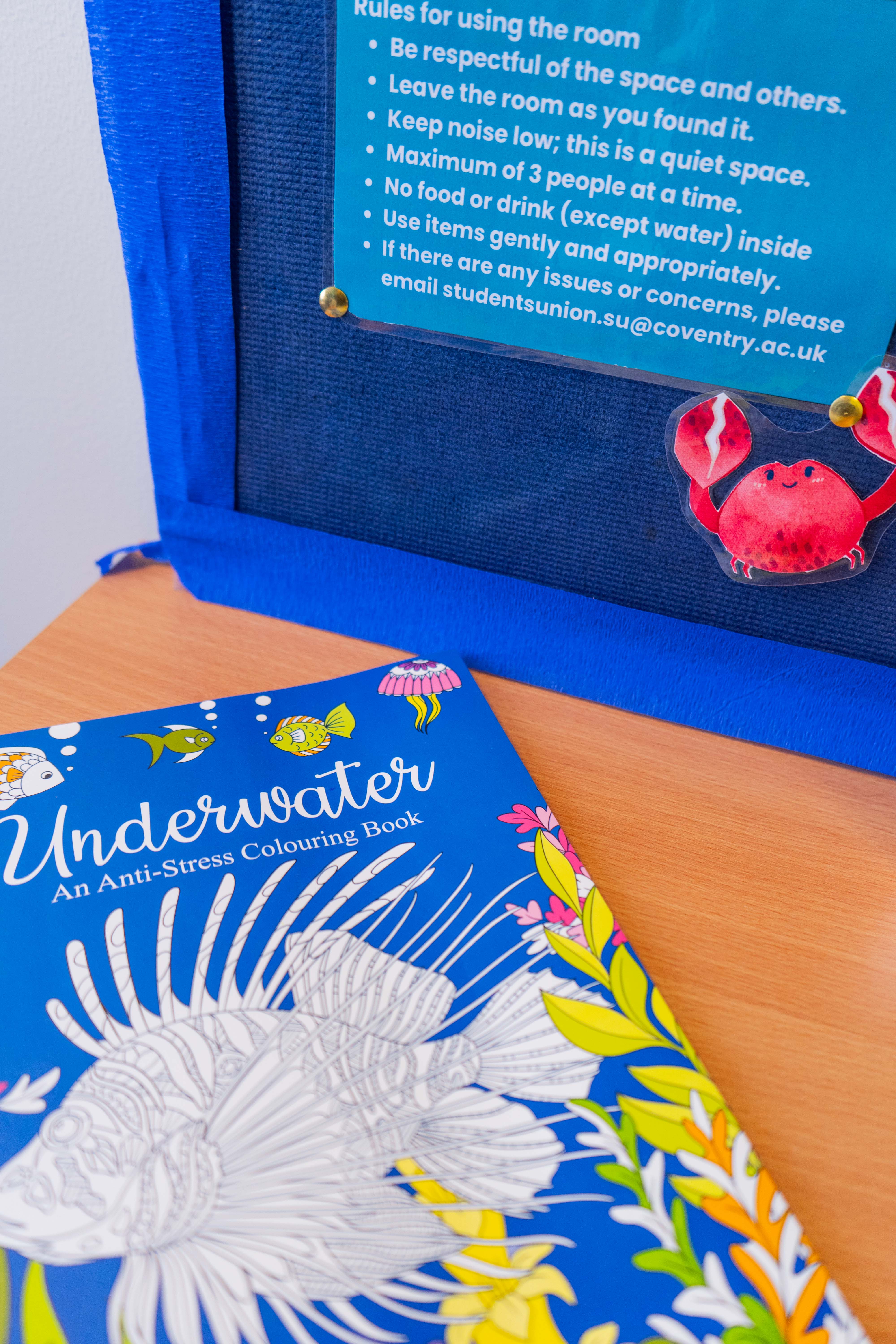 A list of rules pinned on a board and a colouring book placed on a table.