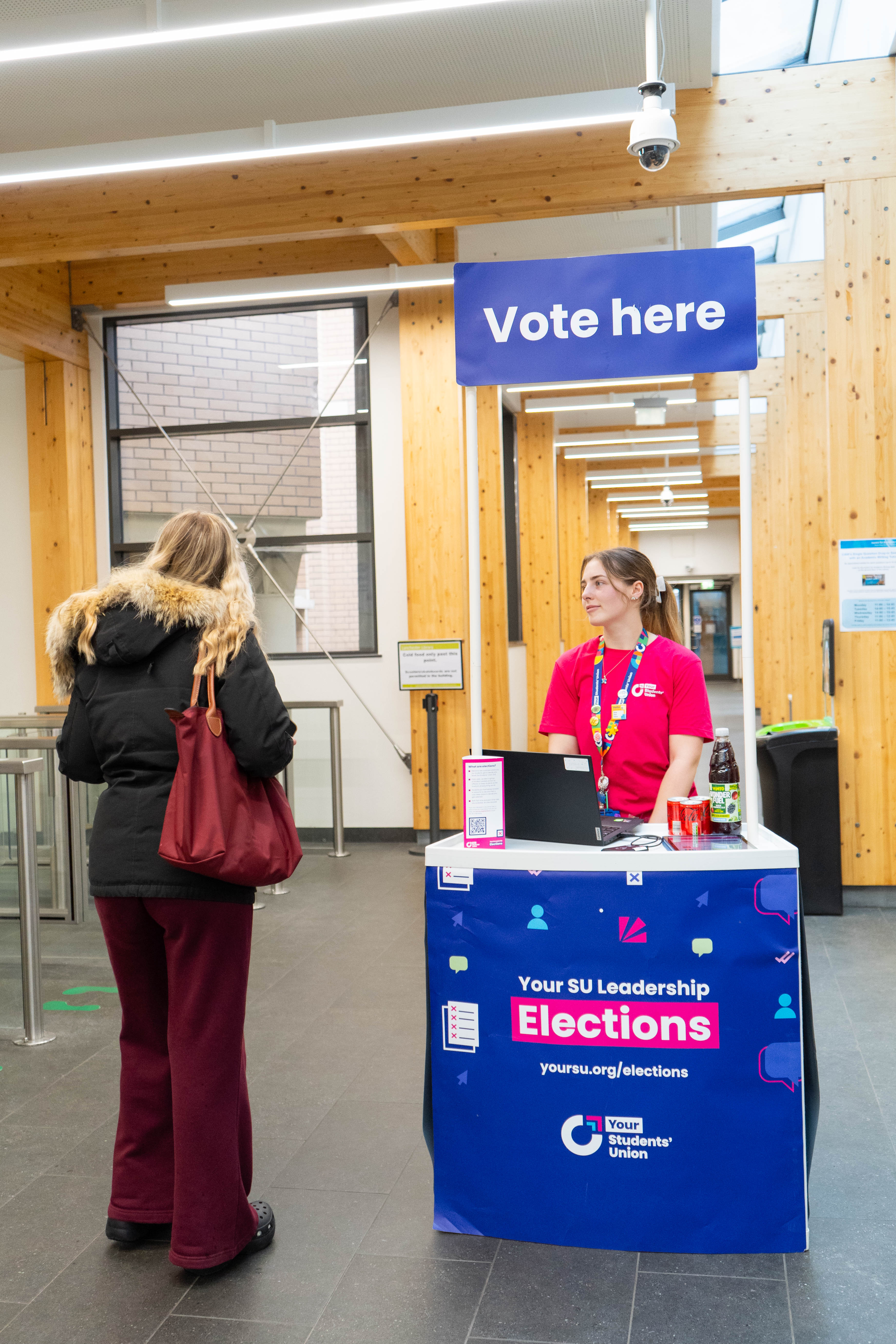 Two people standing and talking in front of a booth that says vote here.
