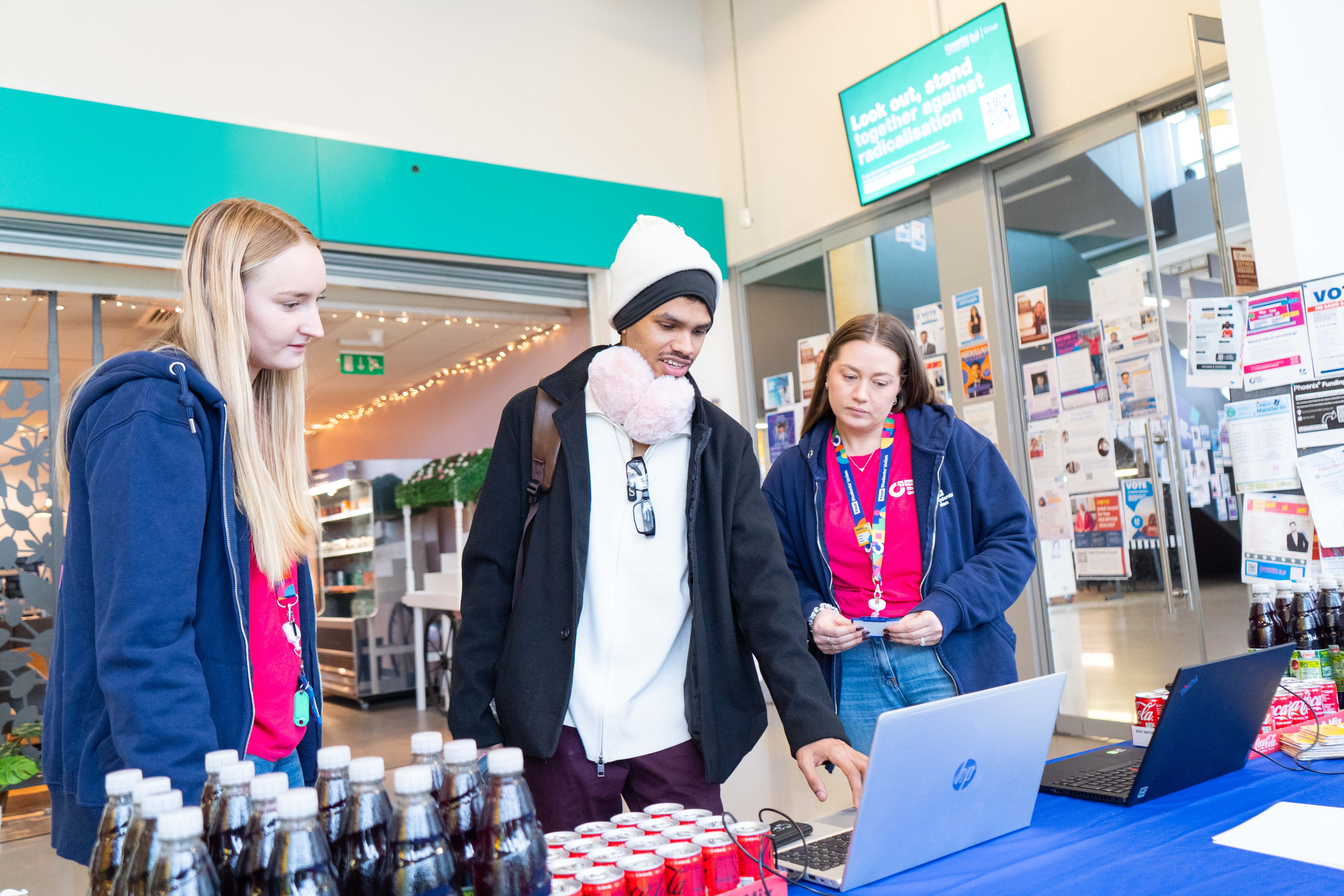 A person being guided through a laptop survey with two Student's Union staff either side of them.