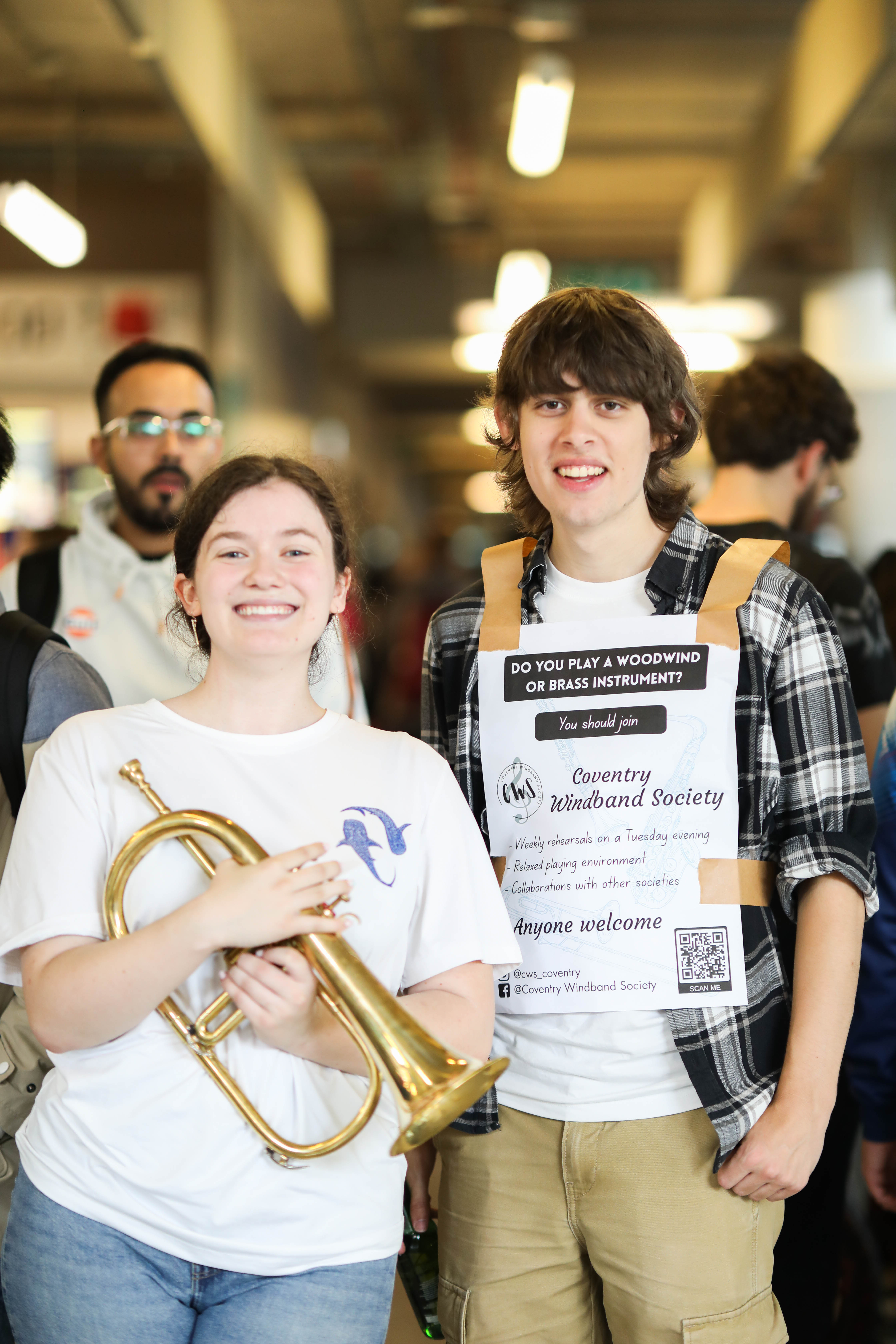 Two people smiling at a camera with one person holding a brass instrument.