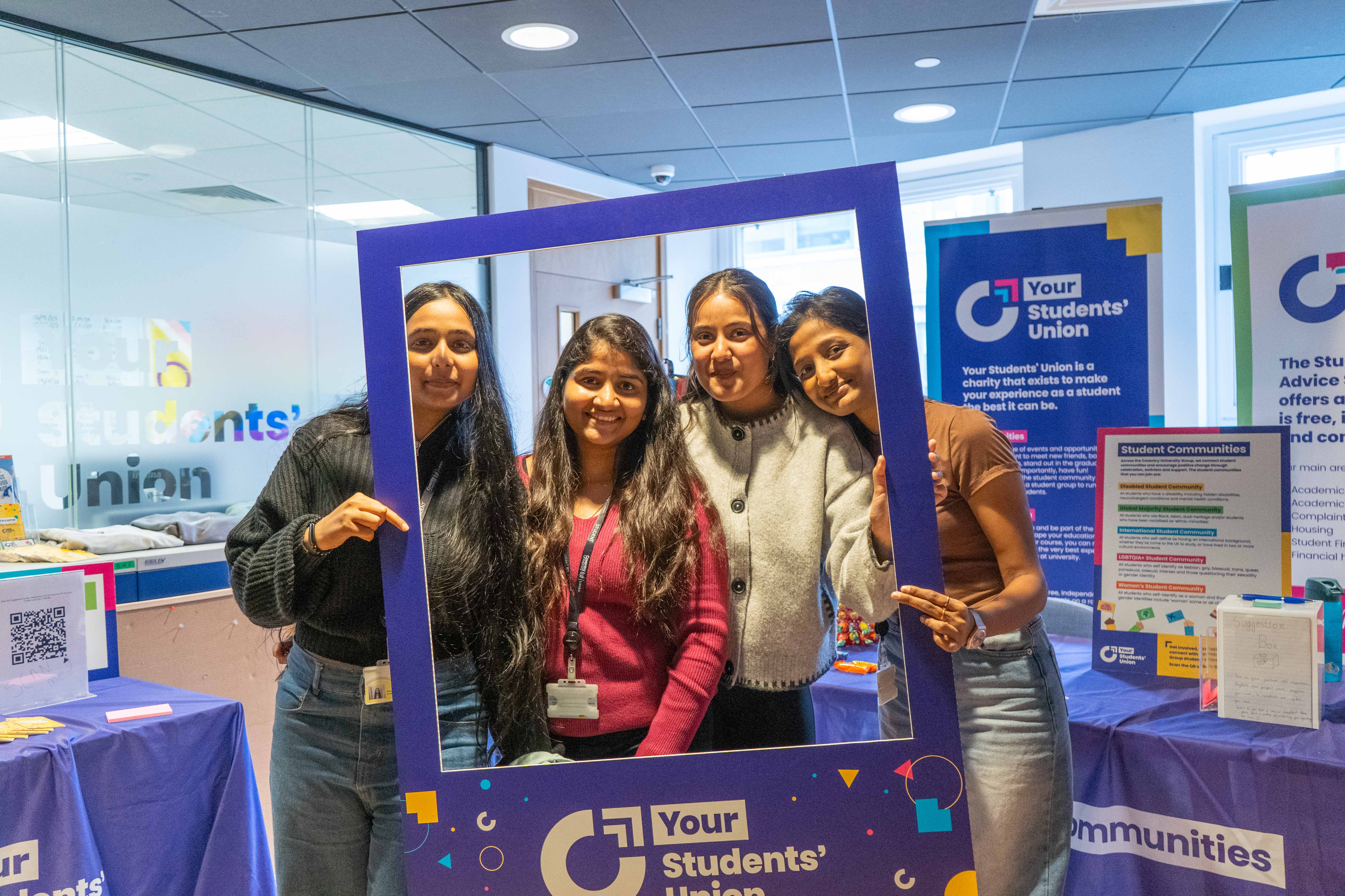 Four people smiling while posing behind a giant photo frame.
