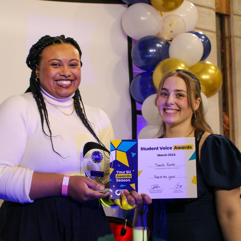 Two people smiling at a camera, with one holding an award.