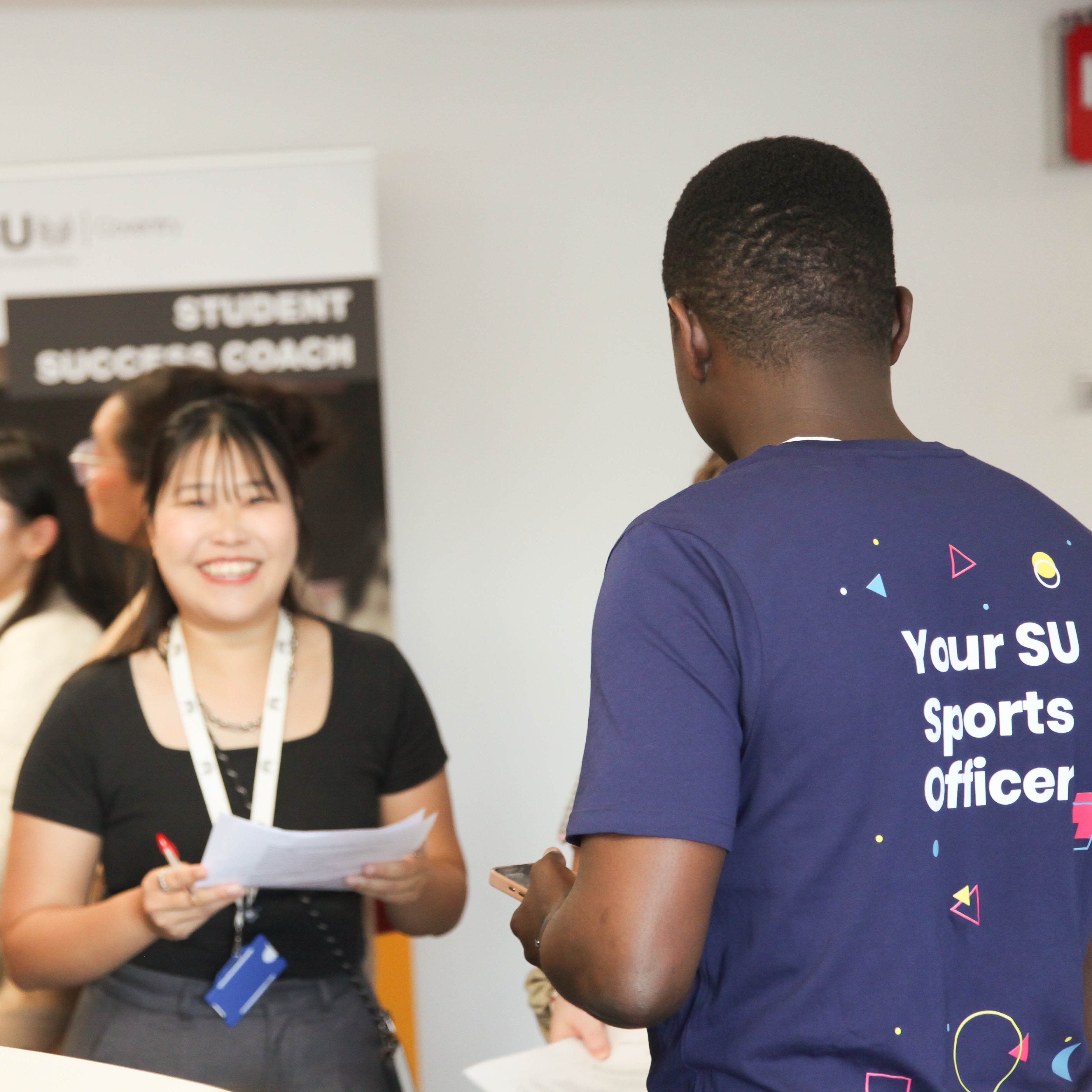 Two people - one wearing a t-shirt with text reading: "Your SU Sports Officer" - engaging in a conversation.
