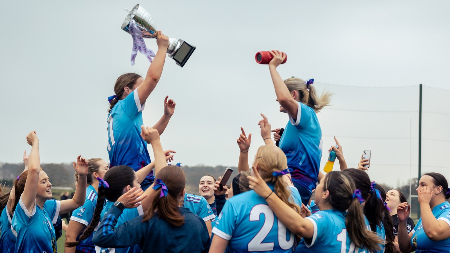 A group of people crowded together, with two people raised higher, holding trophies.